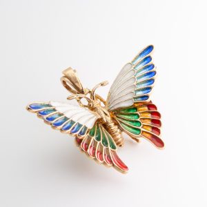 An 18K gold and enamel pendant by J. Roca, featuring a vibrant butterfly design with gold accents and wings in shades of blue, white, green, red, and orange, set against a white background. Joieria Vintage Barcelona