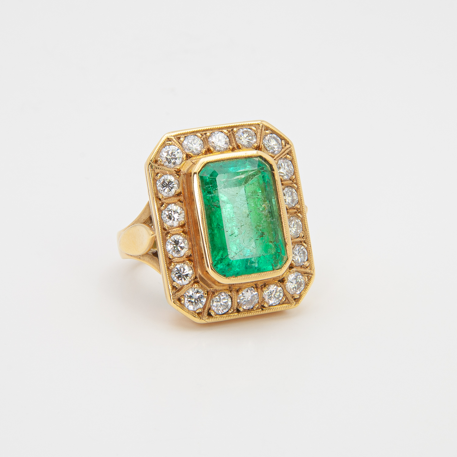 Anillo de oro amarillo 18K con una gran esmeralda rectangular en el centro, rodeada por un borde de diamantes blancos redondos, todo sobre un fondo blanco liso. Joieria Vintage Barcelona
