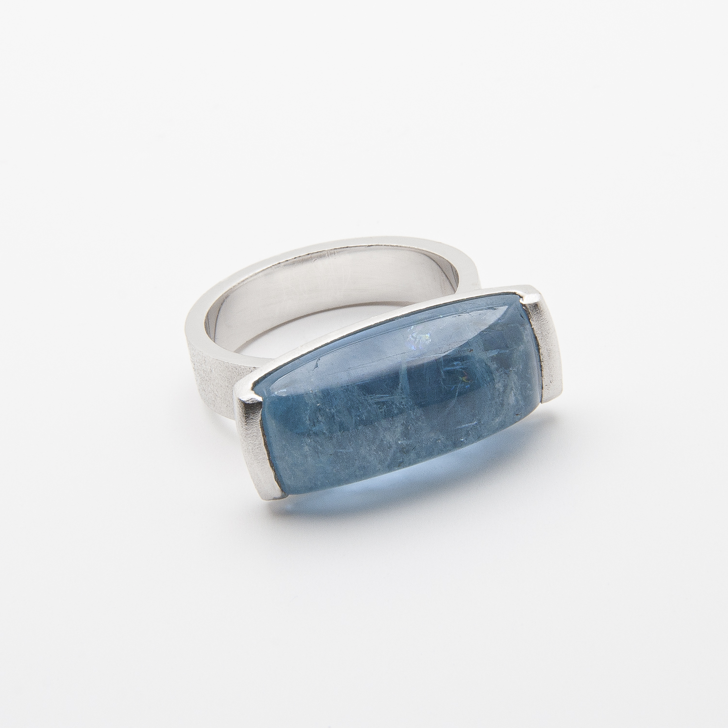 Un anillo de plata que presenta una piedra preciosa aguamarina azul translúcida rectangular en el centro se exhibe sobre un fondo blanco liso. Joieria Vintage Barcelona