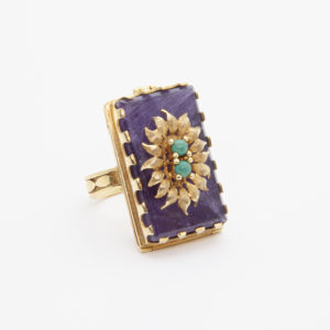 Un anillo de recuerdo de oro amarillo de 18 quilates con amatista y amazonita presenta una gran piedra preciosa violeta rectangular con un diseño floral en cuentas de oro y turquesa en el centro, sobre un fondo blanco liso. Joieria Vintage Barcelona