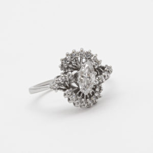 El "Anillo de oro blanco de 18 quilates con diamantes" presenta una piedra central de talla marquesa, intrincadamente rodeada por grupos de varias capas de diamantes más pequeños, todos engastados en oro blanco y exhibidos sobre un fondo blanco. Joieria Vintage Barcelona
