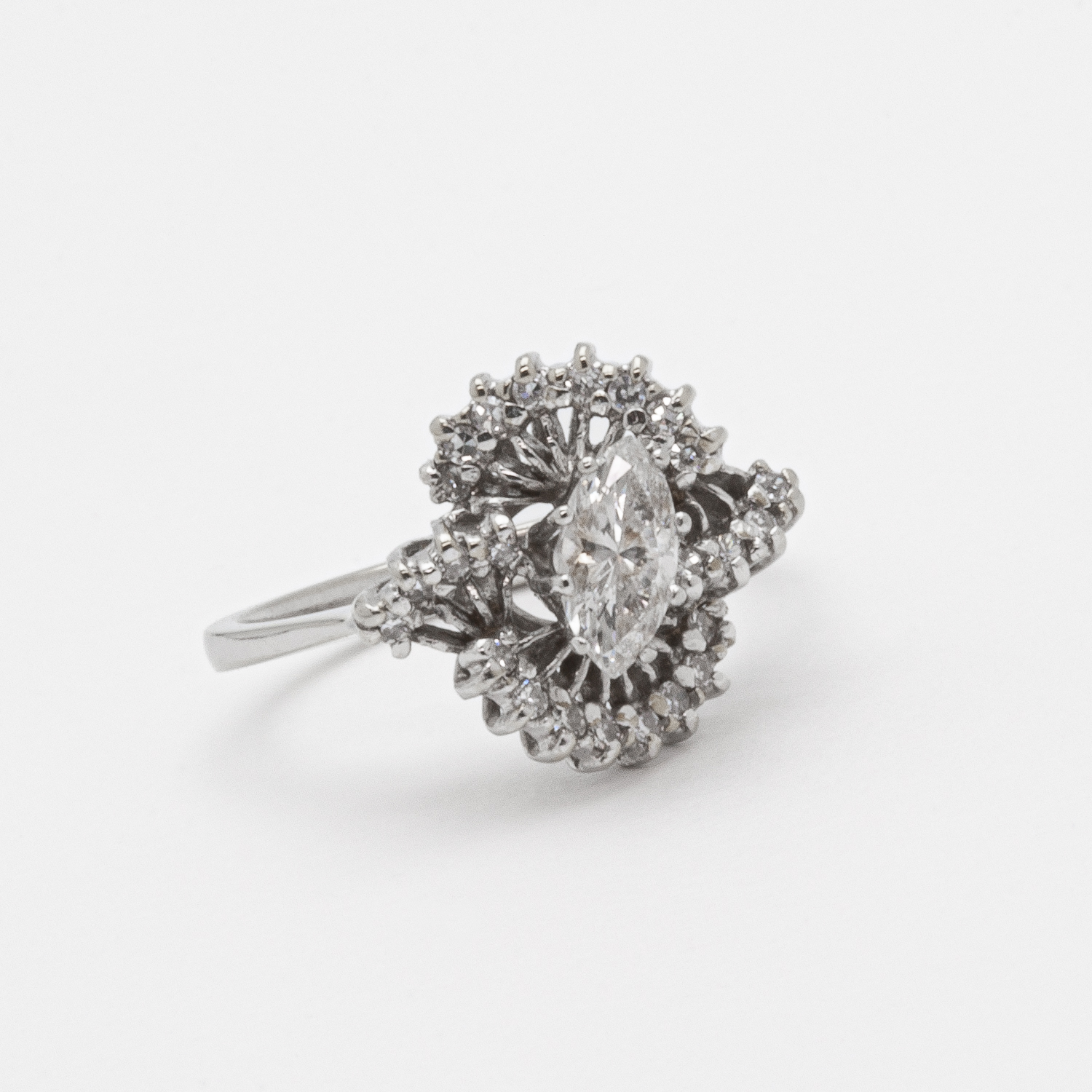 El "Anillo de oro blanco de 18 quilates con diamantes" presenta una piedra central de talla marquesa, intrincadamente rodeada por grupos de varias capas de diamantes más pequeños, todos engastados en oro blanco y exhibidos sobre un fondo blanco. Joieria Vintage Barcelona