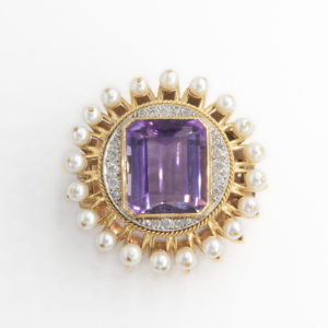 A vintage 1940s brooch crafted from 18K yellow gold and platinum, showcasing a central amethyst diamond surrounded by a circle of small pearls and intricate gold detailing. Joieria Vintage Barcelona