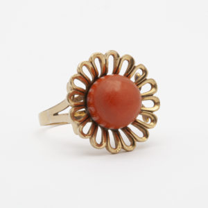 El anillo de oro amarillo de 18 quilates y coral presenta una piedra coral grande y redonda en el centro, rodeada de un diseño intrincado en forma de pétalo. Su apariencia elegante y vintage se destaca sobre un fondo blanco liso. Joieria Vintage Barcelona