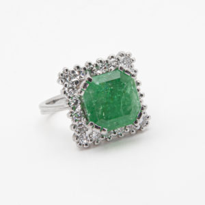 El Anillo de oro blanco de 18 quilates con esmeralda y diamantes exhibe una prominente esmeralda verde de corte cuadrado engastada en plata, rodeada por un halo de pequeños diamantes redondos, todos presentados sobre un sencillo fondo blanco. Joieria Vintage Barcelona