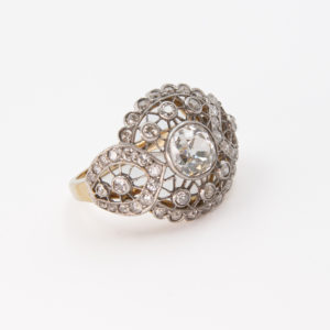 L'Anell Belle Epoque d'or groc de 18K, platí i diamants és un anell d'or vintage que mostra un complex disseny infinit embellit amb nombrosos petits diamants i una pedra preciosa central destacada, tot encaixat sobre un fons blanc senzill. Joieria Vintage Barcelona