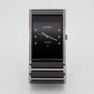 Un sofisticat rellotge de polsera Rado Diastar Jubilé amb un disseny rectangular negre amb una banda metàl·lica i marcadors d'hora de diamant. La cara mostra el text "Rado" i "Jubilé" juntament amb una pantalla de data, vorejada per petits cristalls. Joieria Vintage Barcelona