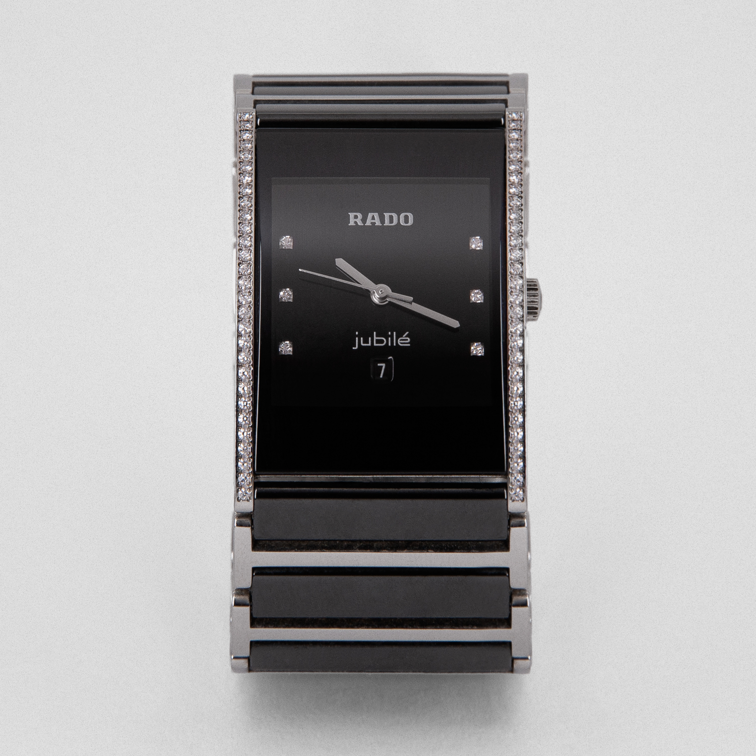 Un sofisticat rellotge de polsera Rado Diastar Jubilé amb un disseny rectangular negre amb una banda metàl·lica i marcadors d'hora de diamant. La cara mostra el text "Rado" i "Jubilé" juntament amb una pantalla de data, vorejada per petits cristalls. Joieria Vintage Barcelona