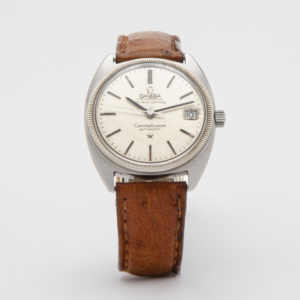 Rellotge Omega Constellation Automàtic d´acer amb corretja de pell marró. L'esfera platejada vintage mostra el logotip de la marca, les paraules "Officially Certified" i "Automatic", juntament amb una finestra de data a la banda dreta de l'esfera. Joieria Vintage Barcelona