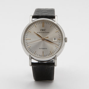 El rellotge de polsera IWC Portofino Acero presenta una caixa platejada elegant, moviment automàtic, esfera blanca, marcadors d'hora daurats, finestra de data a les 3 en punt i una clàssica corretja de cuir negra, bellament presentada sobre un fons llis. Joieria Vintage Barcelona