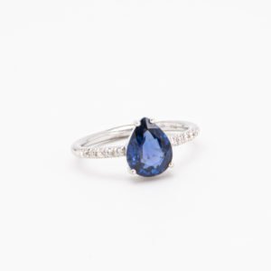 Anell d'or blanc de 18K amb safir i diamants es presenta sobre un fons blanc senzill, amb un safir blau profund en forma de llàgrima al centre, envoltat per petits diamants a la banda. Joieria Vintage Barcelona