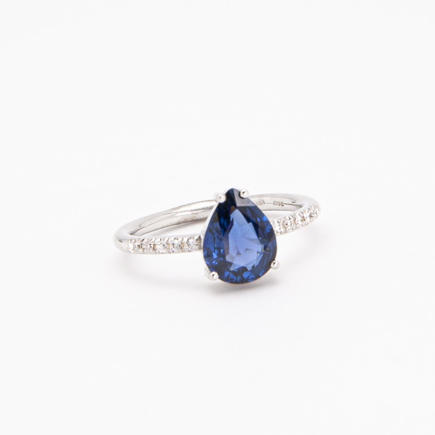 Anell d'or blanc de 18K amb safir i diamants es presenta sobre un fons blanc senzill, amb un safir blau profund en forma de llàgrima al centre, envoltat per petits diamants a la banda. Joieria Vintage Barcelona