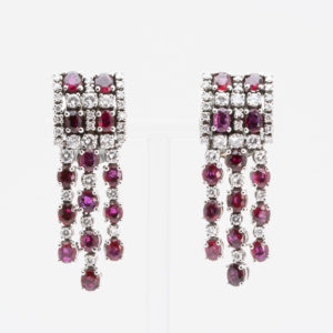 Un par de sofisticados aretes de oro blanco de 18 quilates con diamantes y rubíes, que presentan tres tiras colgantes de piedras preciosas rojas, sobre un fondo blanco liso. Joieria Vintage Barcelona