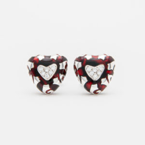 A pair of "Fidia" earrings crafted in 18-karat white gold, featuring heart-shaped designs adorned with spirals of black and red enamel. Each earring showcases a central heart embellished with inlaid diamonds, set against a smooth white background. Vintage Jewelry Barcelona