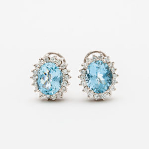 A pair of elegant earrings with large oval aquamarine gemstones surrounded by a halo of sparkling diamonds, set in a silver or white gold metal setting, on a plain white background. Vintage Jewelry Barcelona