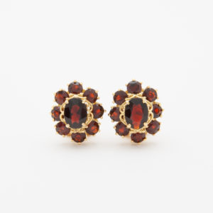 Un par de "Pendientes de granates en oro amarillo 18K" con aretes de oro vintage adornados con piedras preciosas ovaladas de color rojo oscuro y piedras rojas redondas más pequeñas, elaborados en un diseño floral sobre un fondo blanco. Joieria Vintage Barcelona