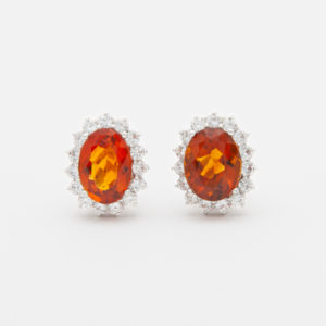 Par de aretes de citrino de forma ovalada, cada uno rodeado por un halo de pequeños diamantes, sobre un fondo blanco. Nombre del producto: Rosetones de oro blanco 18K con diamantes y citrinos. Joieria Vintage Barcelona