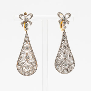 Los pendientes largos Belle Epoque con diamantes son elegantes pendientes en forma de lágrima que se presentan en un soporte. Cada uno tiene un botón en forma de lazo con piedras brillantes, patrones de filigrana elaborados y múltiples piedras preciosas para darle un toque ornamental. Joieria Vintage Barcelona