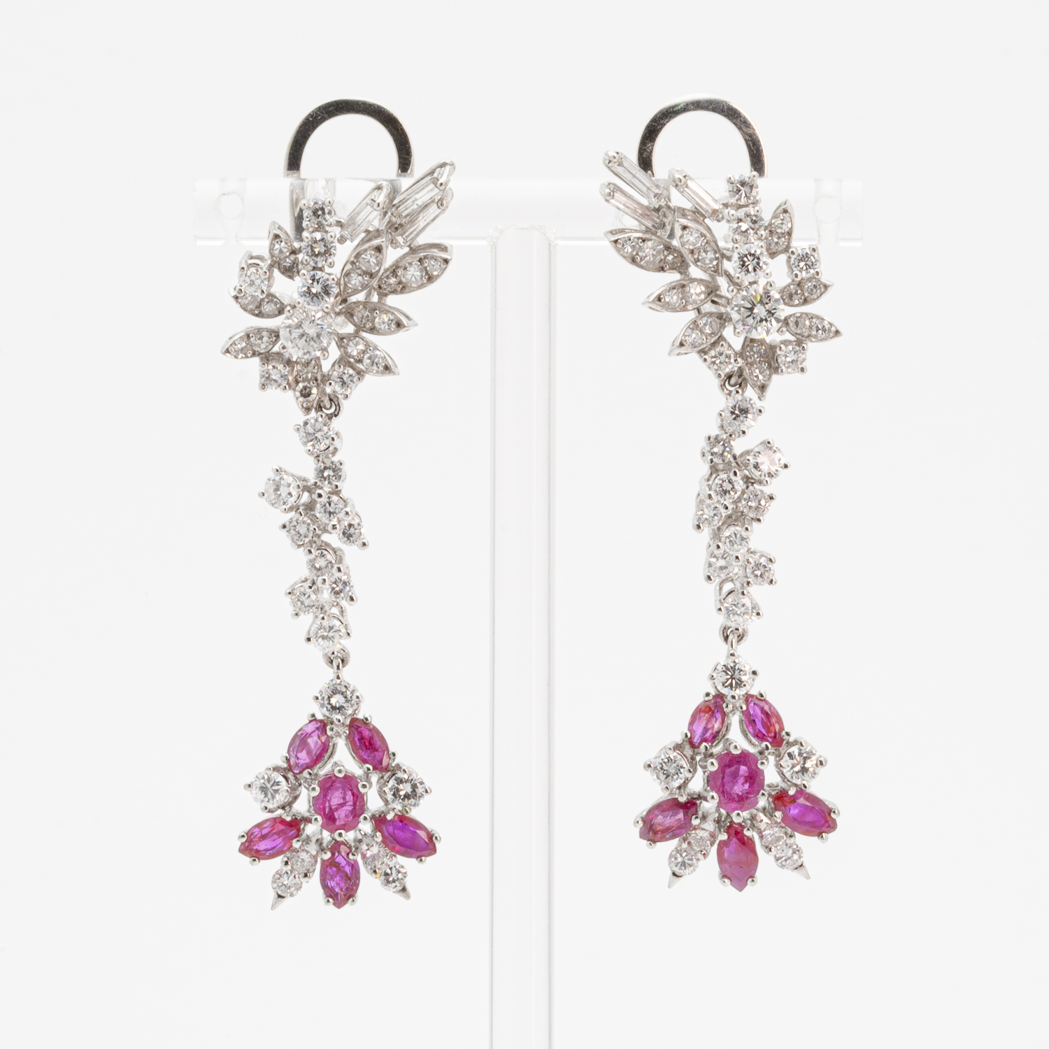 Elegant earrings featuring brilliant diamonds, rubies, and sapphires, crafted in white gold. The design includes a floral cluster at the base that extends to form an intricate, curvilinear trail. They are presented in a clear case. Vintage Jewelry Barcelona