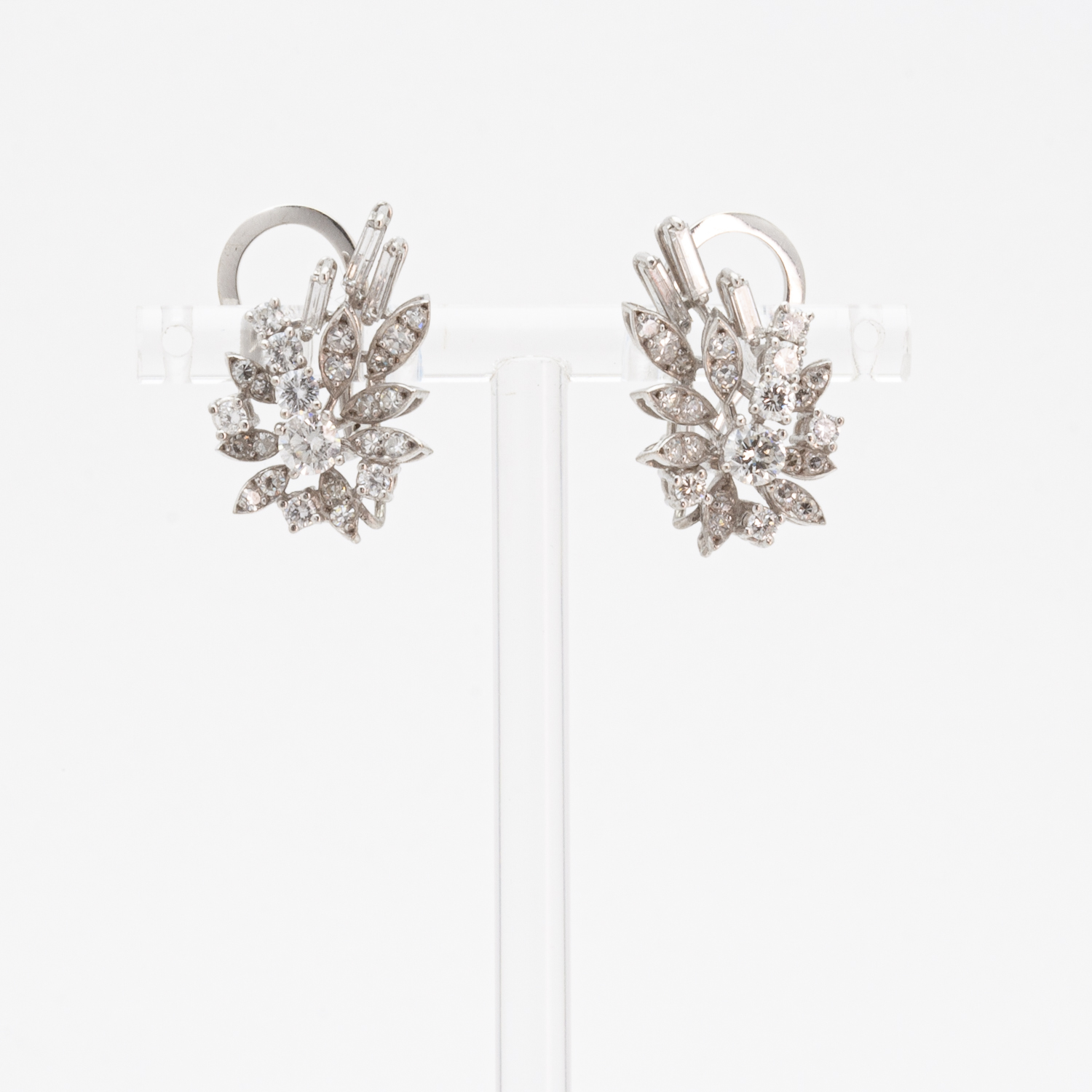 The "three-in-one" gold earrings with diamonds, rubies, and sapphires are presented in a transparent setting. Each piece features an intricate arrangement of petals, lending it a dazzling elegance against a smooth white background. Vintage Jewelry Barcelona
