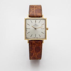 Jaeger-leCoultre Vintage: un rellotge de polsera quadrat amb marc daurat que presenta una esfera blanca amb marcadors d'hora negres mínims, una sola corona i una corretja de cuir marró texturitzat. Joieria Vintage Barcelona