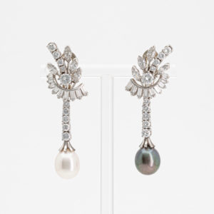 Elegantes aretes con base; uno con una perla blanca y una cascada de diamantes, el otro con una perla negra y diamantes similares. Oficialmente llamados "Pendientes de oro blanco con perla japonesa, de Tahití y diamantes". Joieria Vintage Barcelona