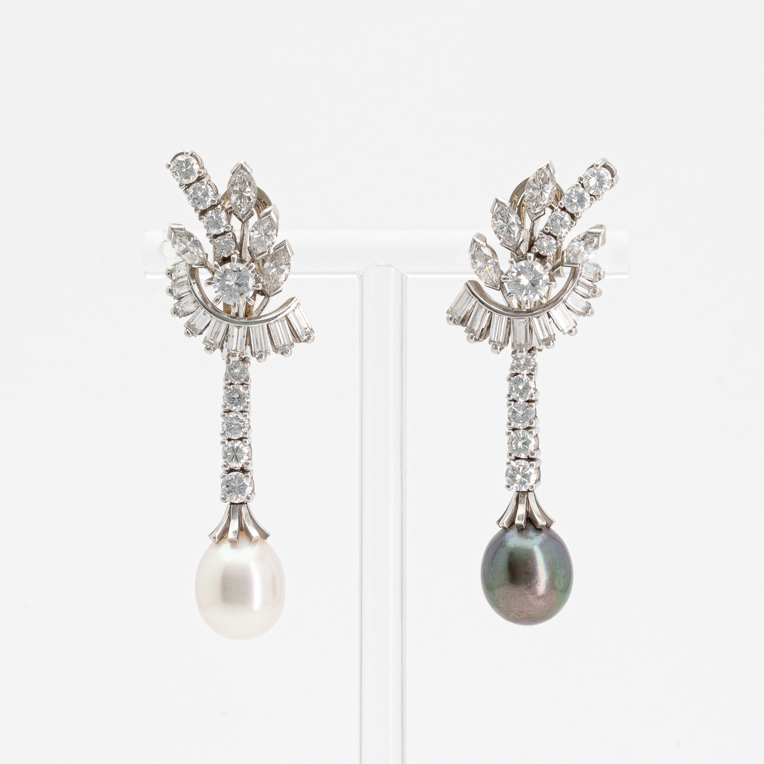 Elegantes aretes con base; uno con una perla blanca y una cascada de diamantes, el otro con una perla negra y diamantes similares. Oficialmente llamados "Pendientes de oro blanco con perla japonesa, de Tahití y diamantes". Joieria Vintage Barcelona