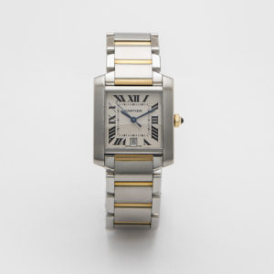 El Cartier Tank Française es un reloj de pulsera de plata y oro con una esfera rectangular, números romanos negros, una pequeña ventana de fecha en la parte inferior y un brazalete de acero inoxidable y eslabones en tono dorado. Joieria Vintage Barcelona