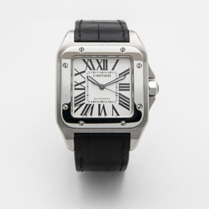 El Cartier Santos 100 XL compta amb un bisell quadrat platejat, una esfera blanca amb números romans negres i agulles platejades. Inclou una corretja de pell negra i porta la inscripció "Cartier" i "Automàtic" a l'esfera. Joieria Vintage Barcelona