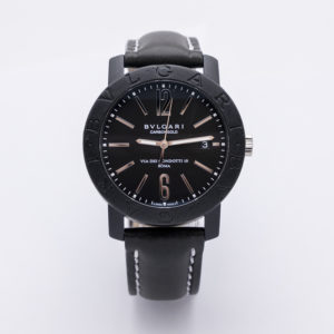 El rellotge de polsera Bulgari Carbongold Via Condotti BB 40 CL, amb corretja de pell negra amb costures blanques i detalls platejats, es presenta sobre un fons blanc. L'esfera mostra la data i llueix les inscripcions "BVLGARI" i "ROMA". Joieria Vintage Barcelona