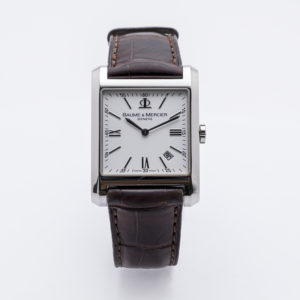 El Baume & Mercier Hampton és un rellotge de polsera d'esfera quadrada amb esfera blanca, números romans, indicador de data i una corretja de cuir marró sobre un fons blanc. Joieria Vintage Barcelona