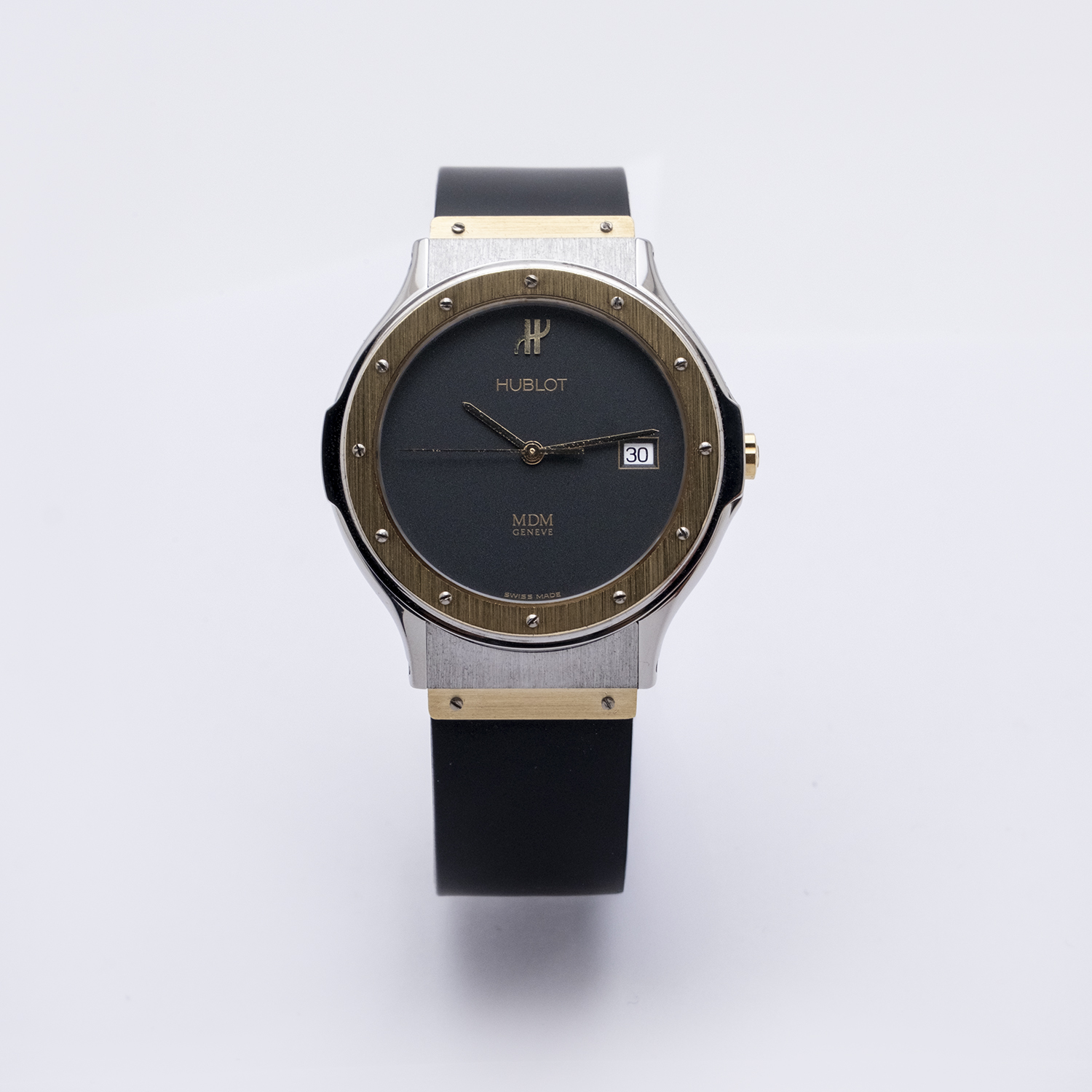 Un rellotge de polsera Hublot MDM Classic de 35 mm amb corretja negra, bisell rodó daurat amb cargols, esfera negra i finestra de data que mostra "30", fotografiat sobre un fons blanc llis. Joieria Vintage Barcelona