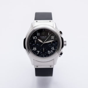 El cronògraf automàtic Hublot MDM compta amb una caixa platejada, una esfera rodona negra amb números blancs, tres subesferes i una corretja de cautxú negra, tot sobre un fons blanc llis. Joieria Vintage Barcelona