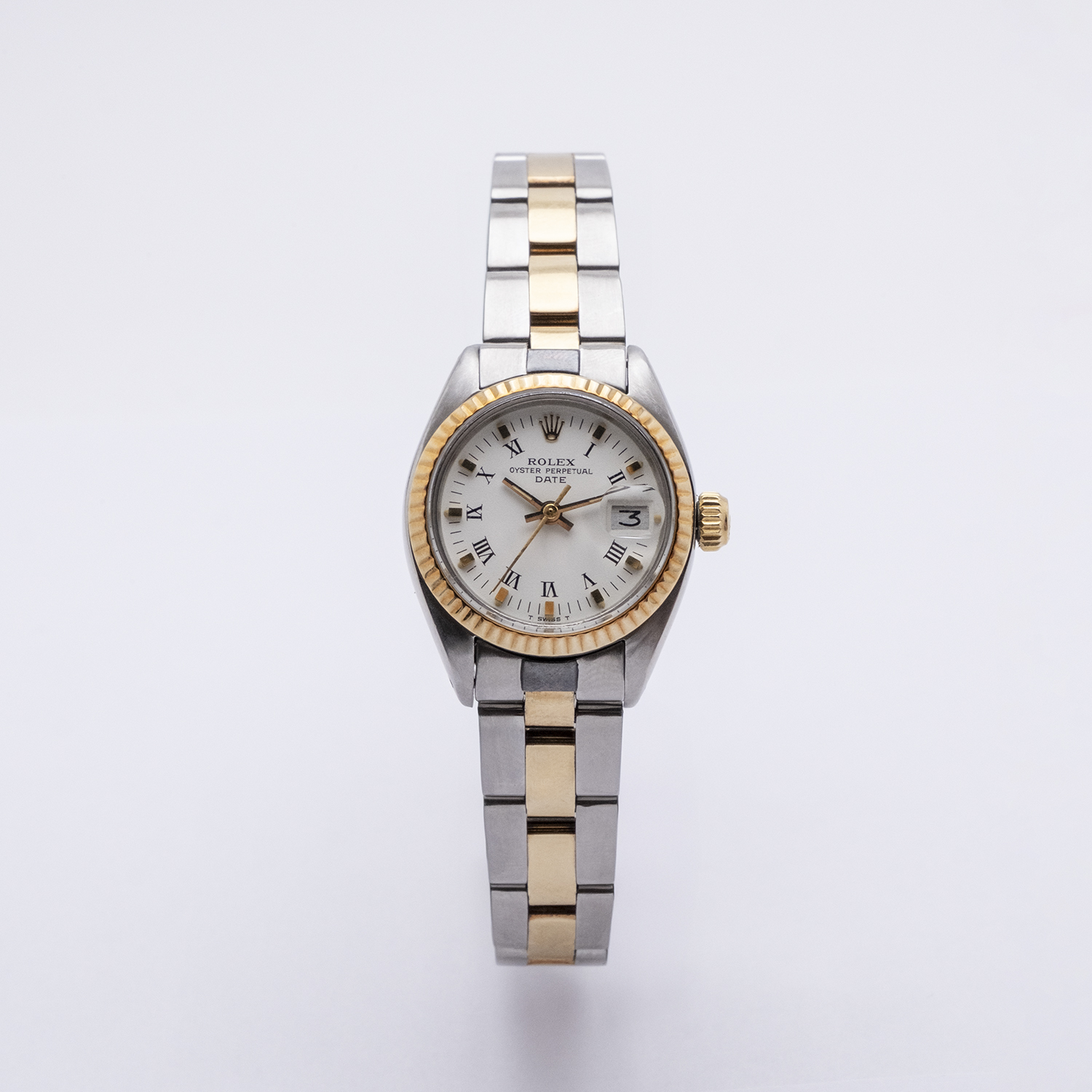 El Rolex Lady Oyster Perpetual Date es un reloj de pulsera de lujo que cuenta con una correa de metal de dos tonos plata y oro, una esfera blanca redonda con números romanos, bisel dorado, ventana de fecha y la marca “Rolex” visible en la cara. Joieria Vintage Barcelona