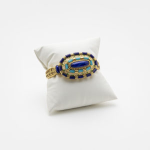 An 18k gold bracelet with lapis lazuli, turquoise and enamels is displayed on a padded white stand, highlighting the beauty of the handcrafted jewelry against a white background. Vintage Jewelry Barcelona