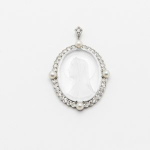 Colgante de oro blanco de 18 quilates con un cuarzo tallado que representa el perfil de una mujer con velo, rodeado de diamantes y perlas, sobre un fondo blanco liso. Joieria Vintage Barcelona