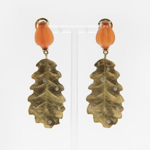 Los Pendientes Vasari de oro 18k, con diamantes y cornalina son pendientes colgantes con remates de cuentas naranjas y grandes colgantes dorados en forma de hoja adornados con piedras preciosas, que se muestran sobre un soporte transparente sobre fondo blanco. Joieria Vintage Barcelona
