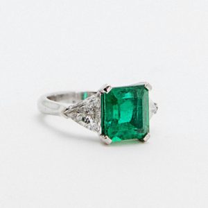 Anillo de esmeralda, diamantes y oro blanco 18k firmado por Ernest Oriol, con una gran esmeralda cuadrada central y dos diamantes triangulares a los lados, exhibido sobre fondo blanco. Joieria Vintage Barcelona