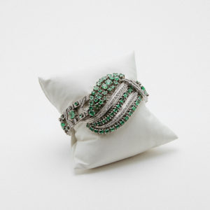 Pulsera de platino engastada con diamantes y esmeraldas, presentada en un cojín de satén blanco sobre fondo liso. Joieria Vintage Barcelona