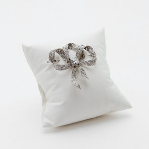An Art Deco platinum brooch with exposed diamonds on a small white cushion against a plain white background. Vintage Jewelry Barcelona