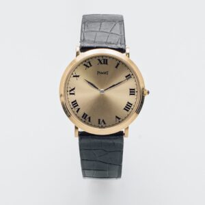 El Piaget Or 18K és un rellotge de polsera d'or amb esfera rodona, números romans negres i polsera de pell negra. Les agulles apunten cap a les 10.08 sobre un fons blanc llis.  Joieria Vintage Barcelona