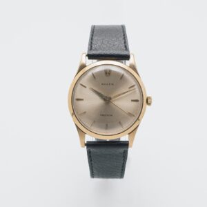 El Rolex Precision és un rellotge de polsera vintage d´or amb esfera beix, marcadors d´hora mínims i corretja de pell negra, sobre un fons blanc llis. Joieria Vintage Barcelona